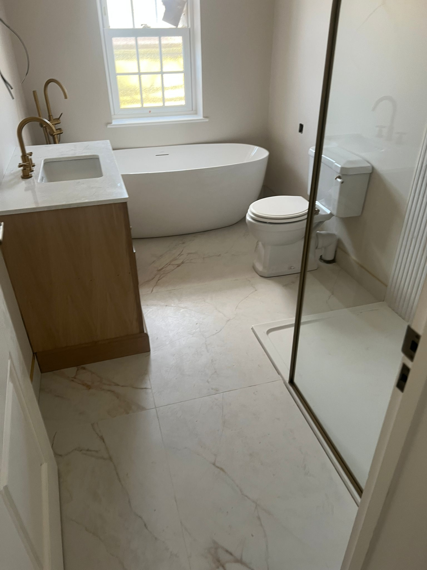 Freestanding bath, marble floor tiles and brass floor-mounted taps — Avanza bathroom installation, Essex