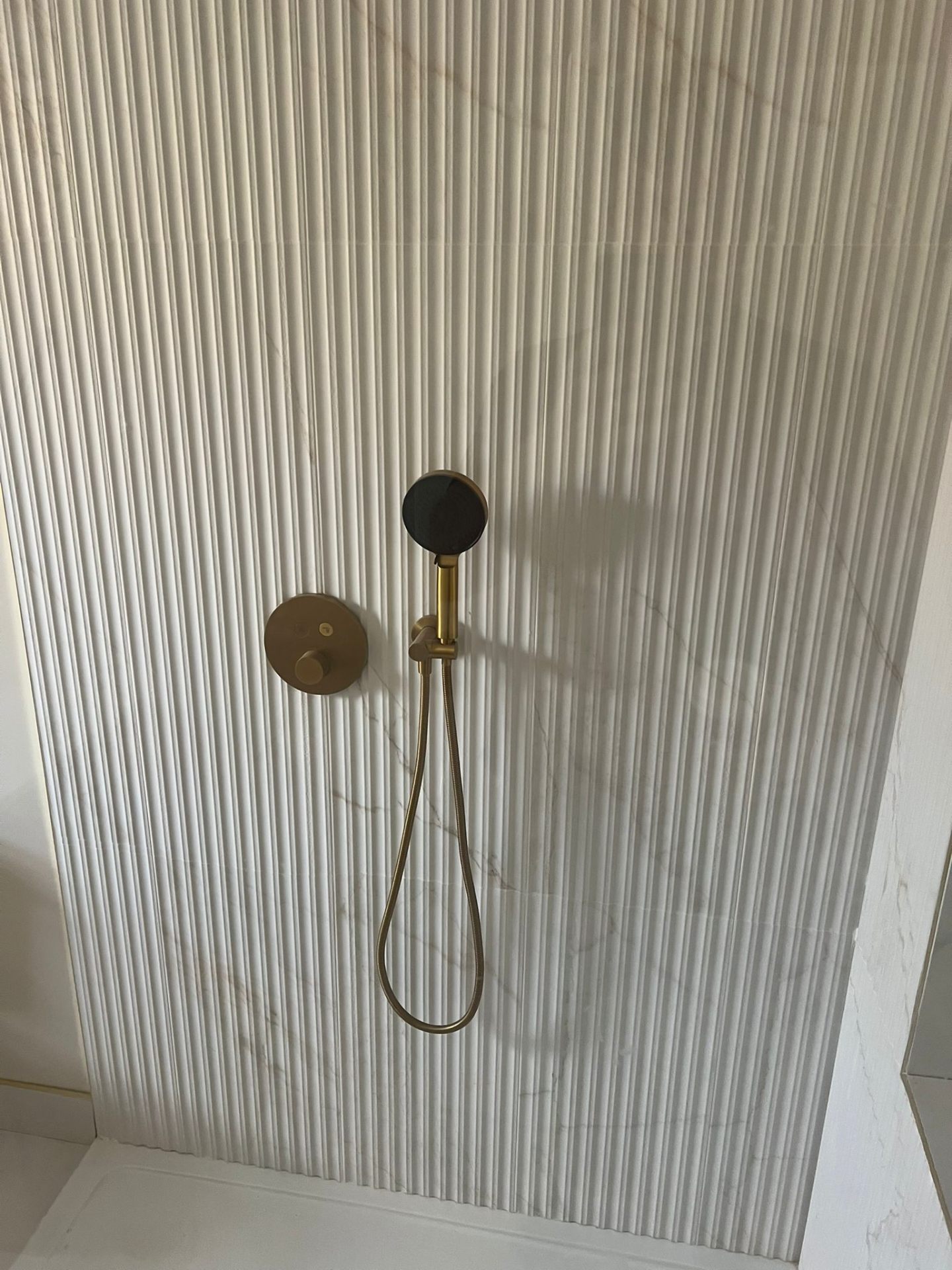 Shower with brass handset over reeded marble tiles, Essex