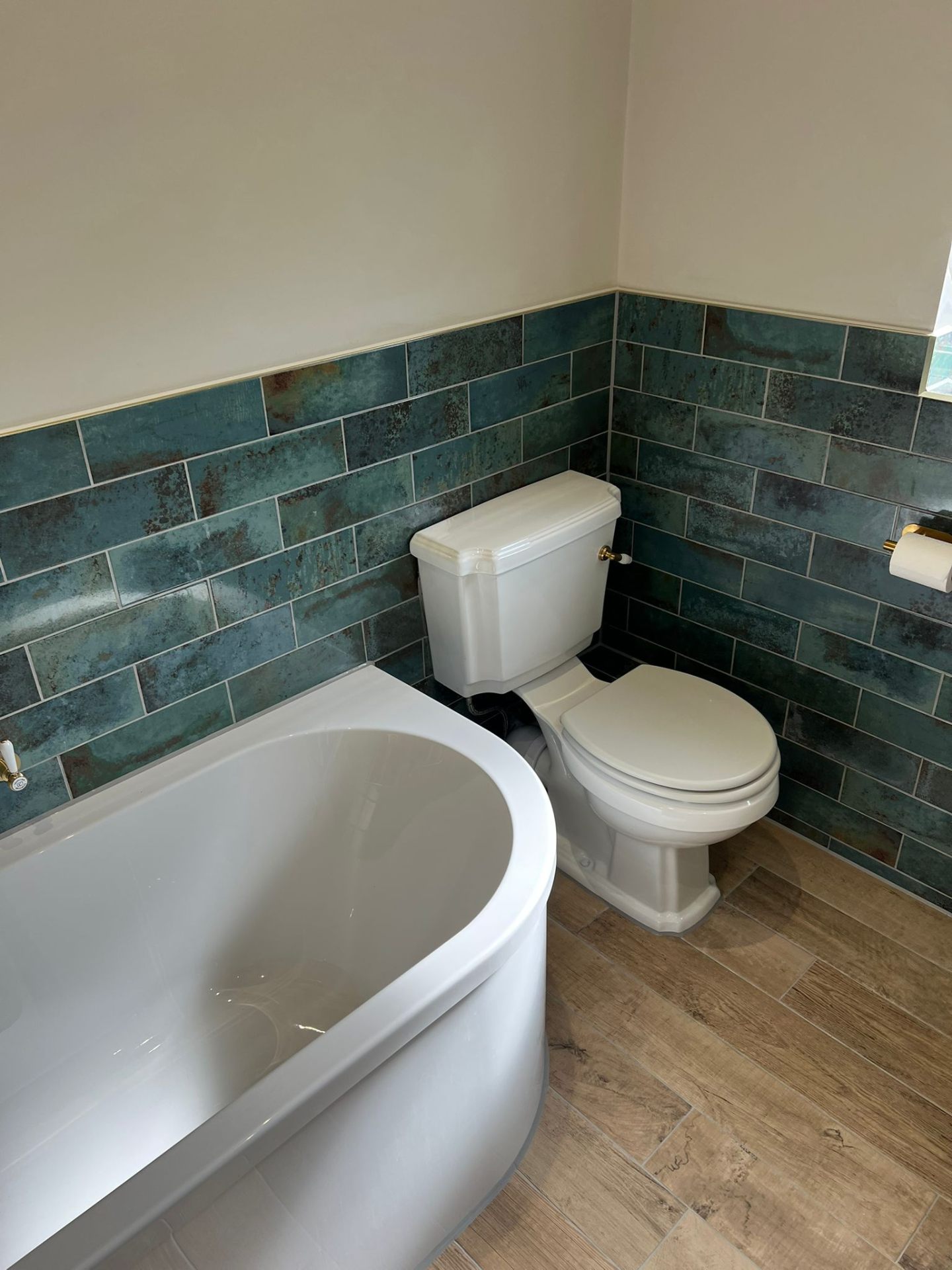 Bathroom with freestanding bath, toilet, teal tiles and wood floor, Essex
